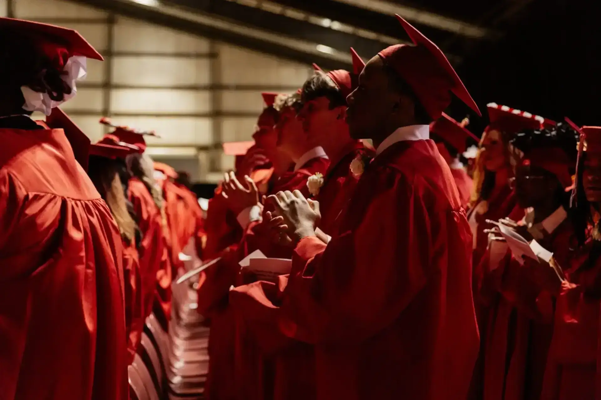 Los graduados con togas y birretes rojos se colocan en filas, mirando al frente.