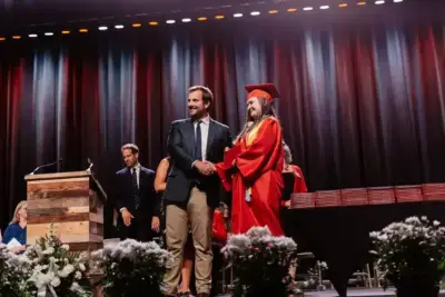 Un graduado con toga roja estrecha la mano de un hombre sonriente en una ceremonia de graduación.