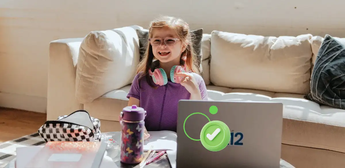 Una estudiante de primaria trabajando con su ordenador portátil en casa con unos auriculares rosas.